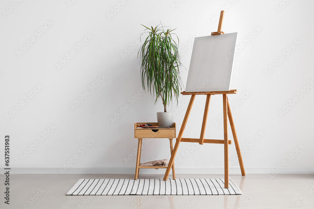 Wooden easel with blank canvas near grey wall