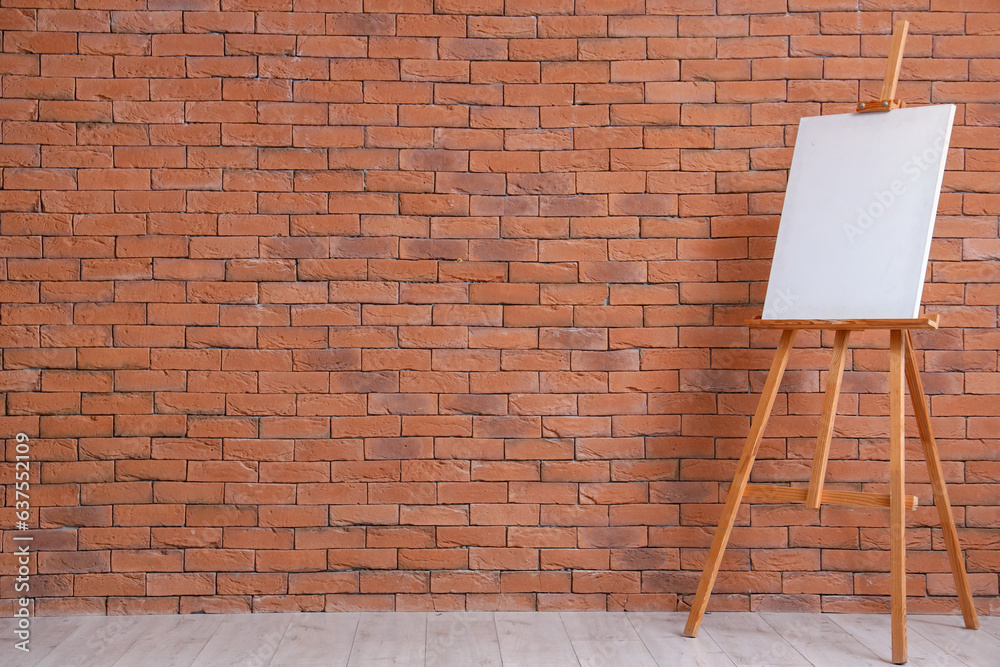 Wooden easel with blank canvas near brown brick wall