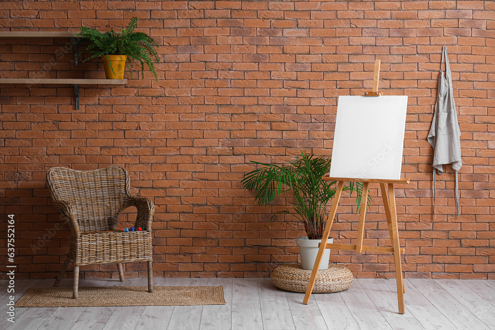 Wooden easel with blank canvas near brown brick wall