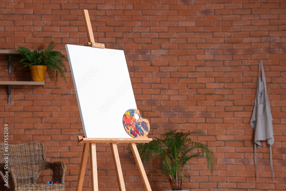 Wooden easel with blank canvas near brown brick wall