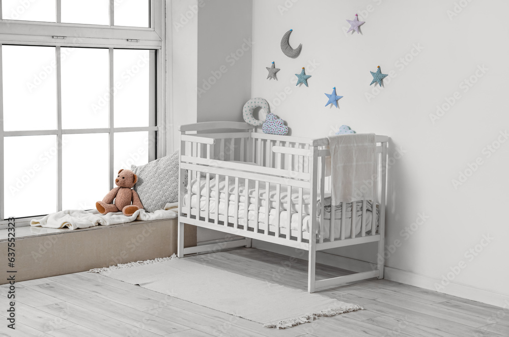 Interior of childrens room with crib and teddy bear near window