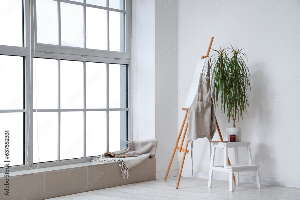 Wooden easel with blank canvas near white wall