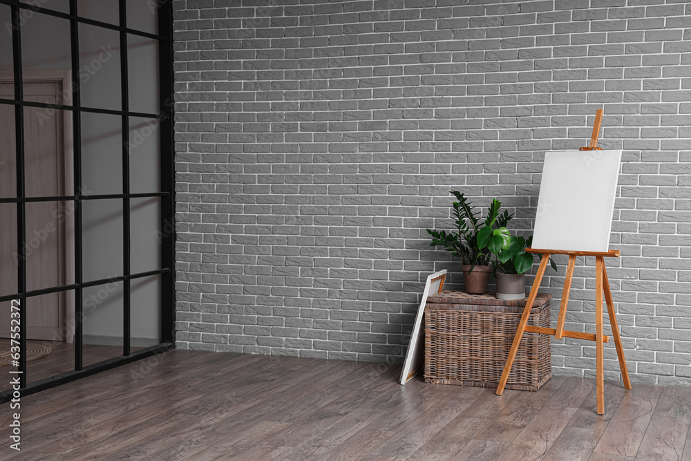 Wooden easel with blank canvas near grey brick wall