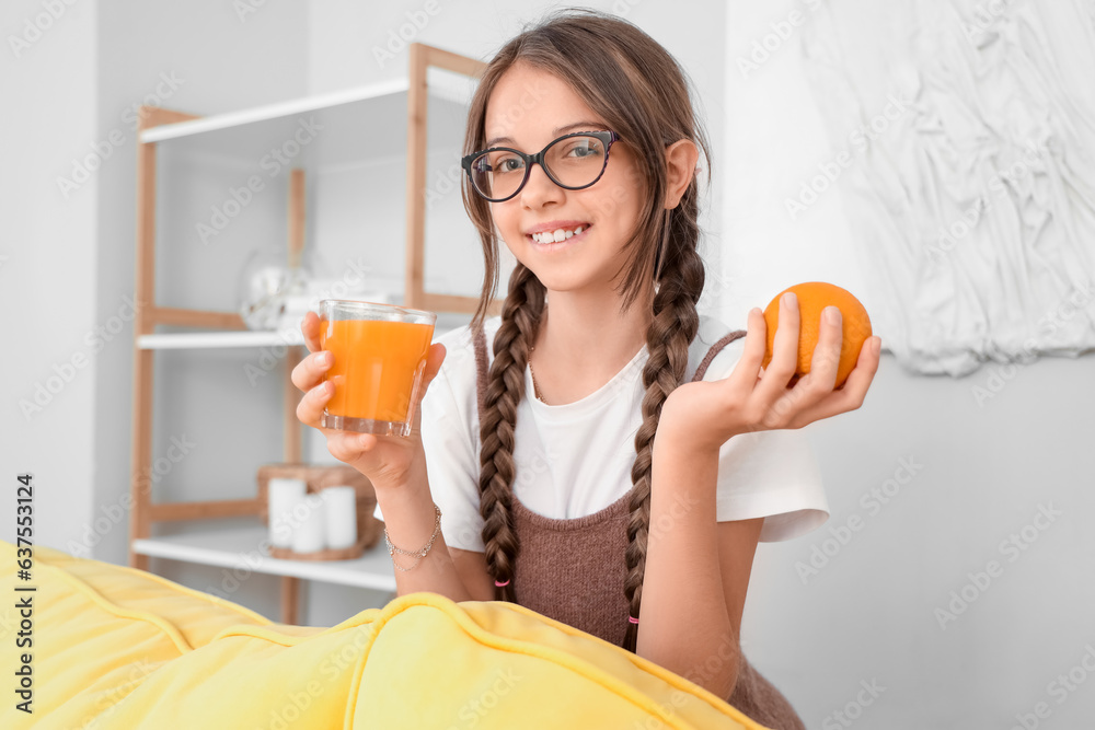 Little girl with glass of juice and orange at home