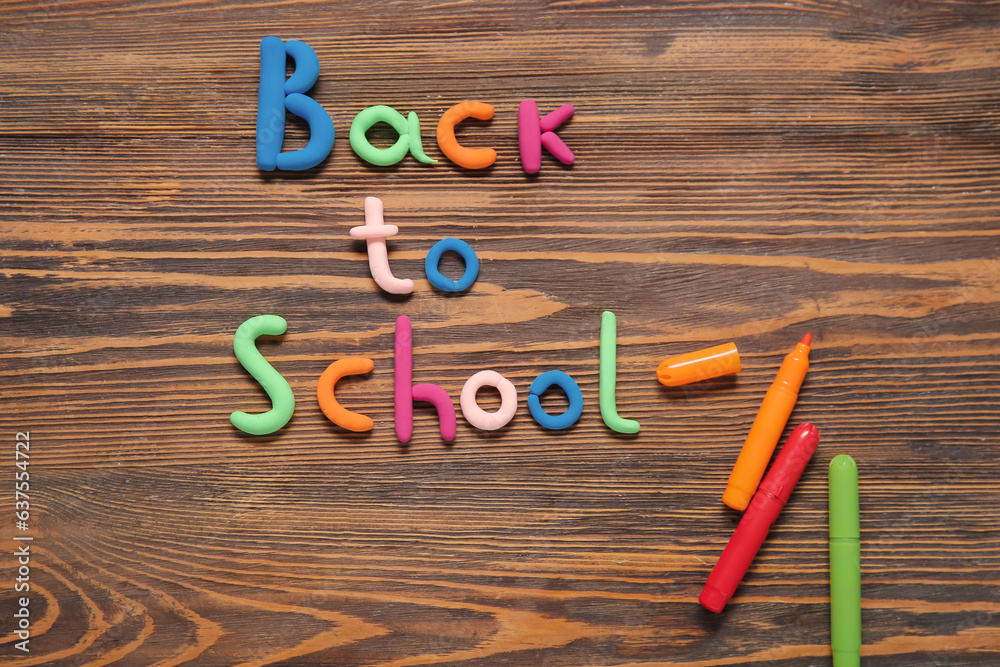 Text BACK TO SCHOOL and markers on wooden background