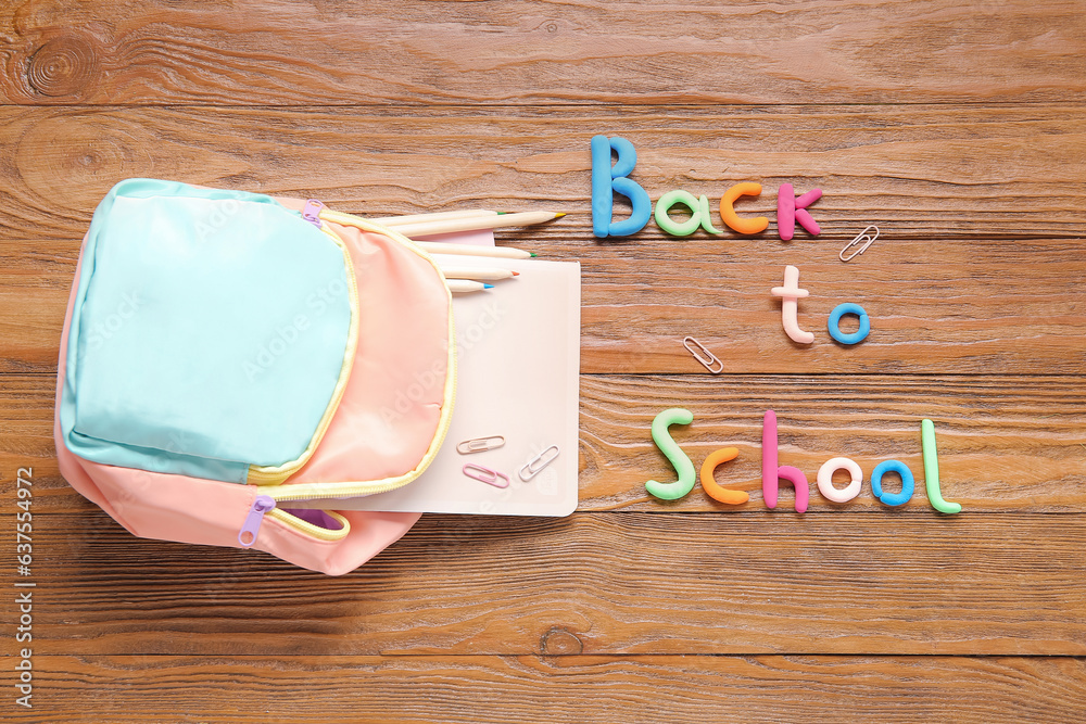 Text BACK TO SCHOOL, backpack and stationery on wooden background