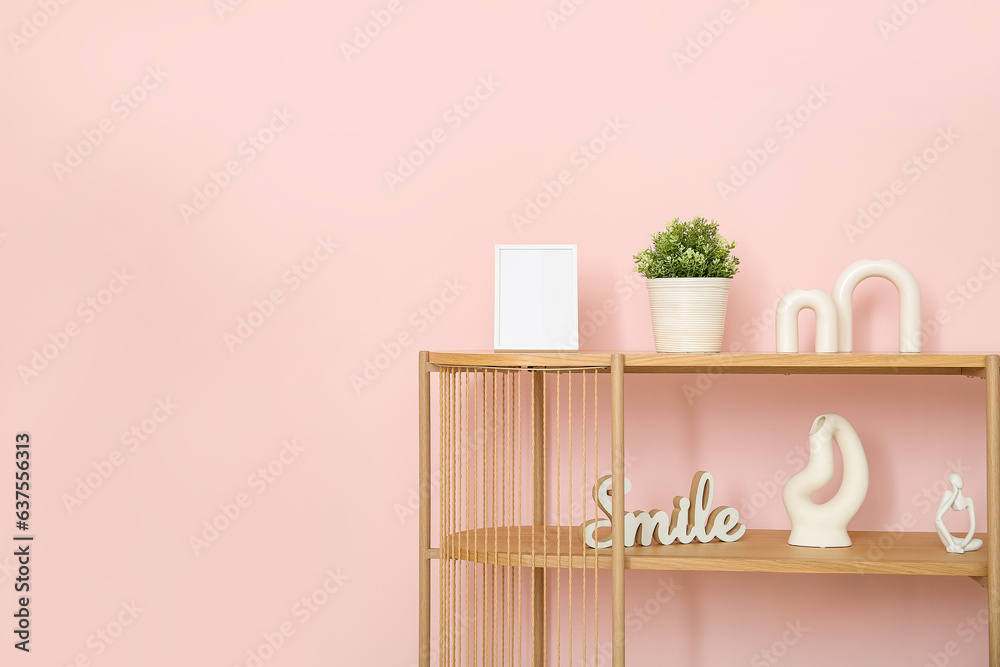 Wooden shelving unit with blank frame and decor near pink wall