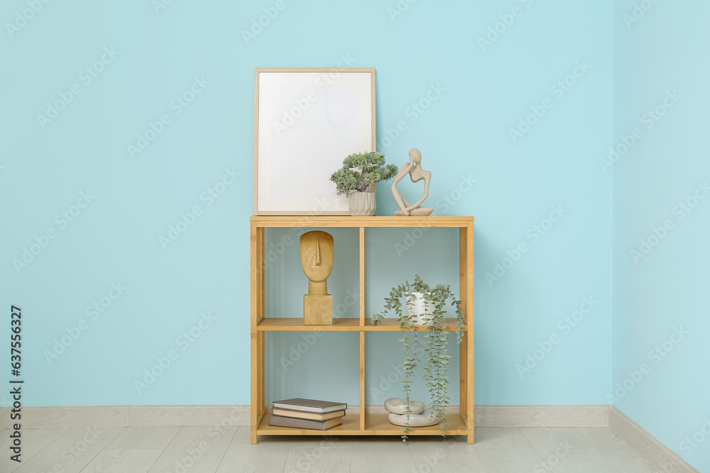 Shelving unit with blank frame and decor near blue wall