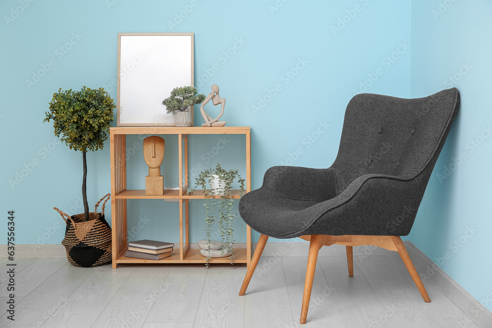 Shelving unit with blank frame and armchair near blue wall