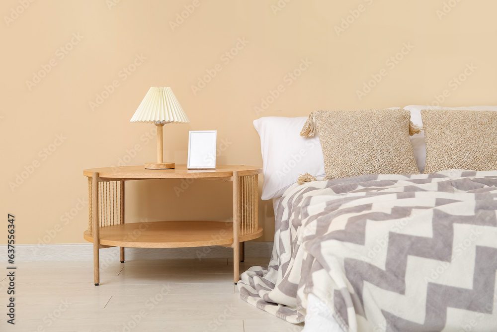 Wooden bedside table with blank frame and lamp in bedroom