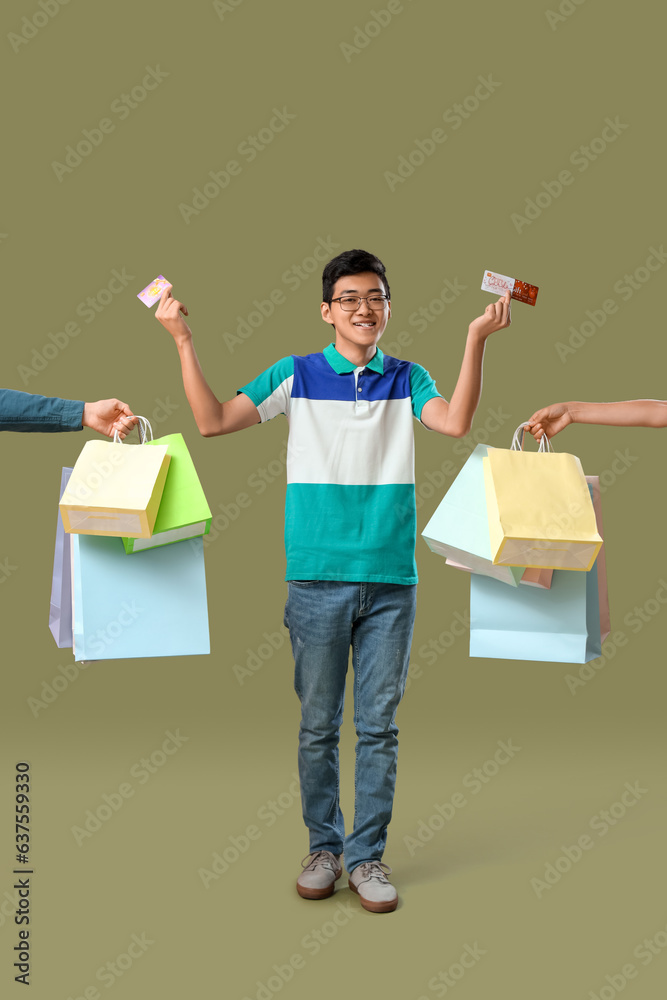 Young Asian man with gift cards and shopping bags on green background