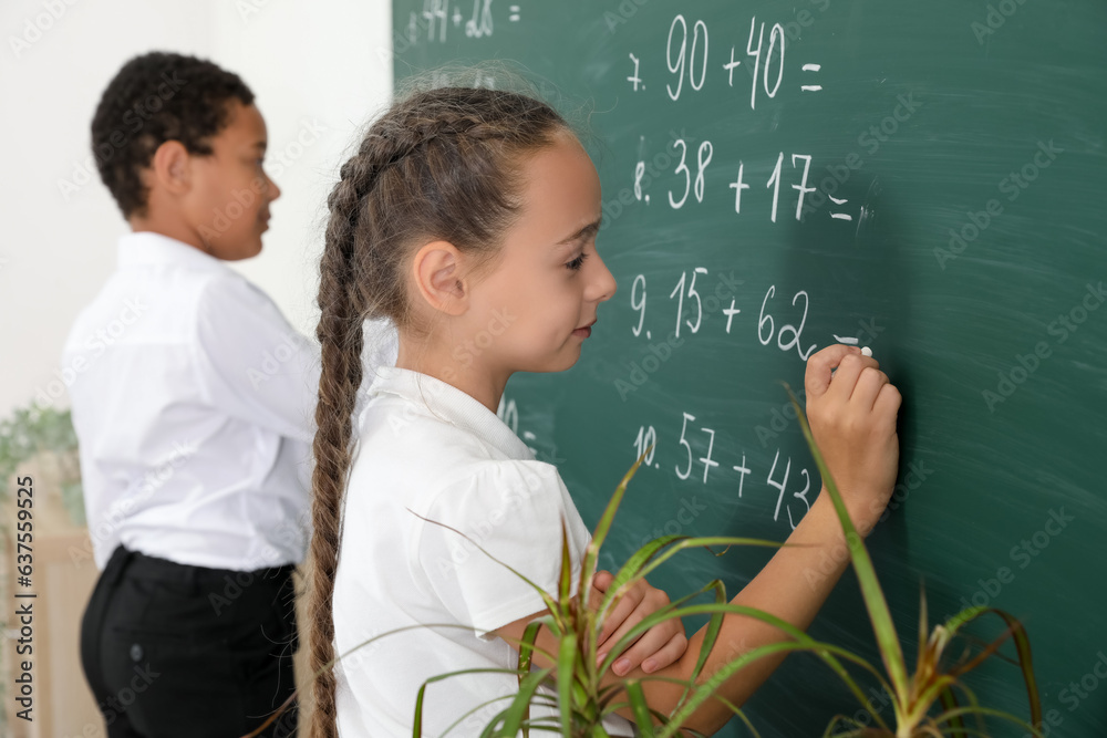 Little classmates writing on chalkboard in classroom