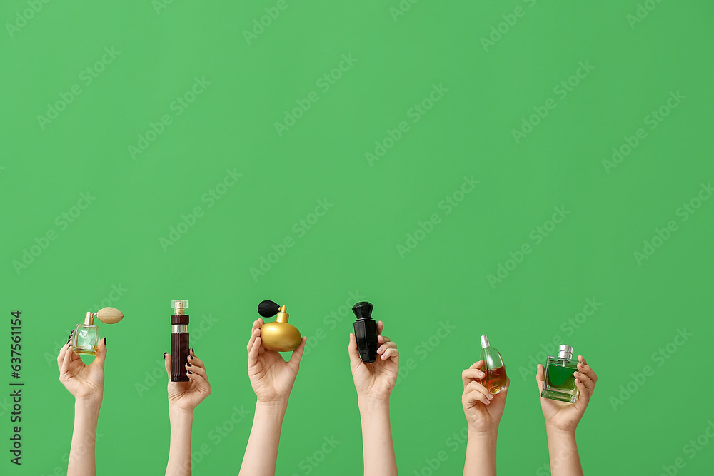 Female hands holding different perfumes on green background