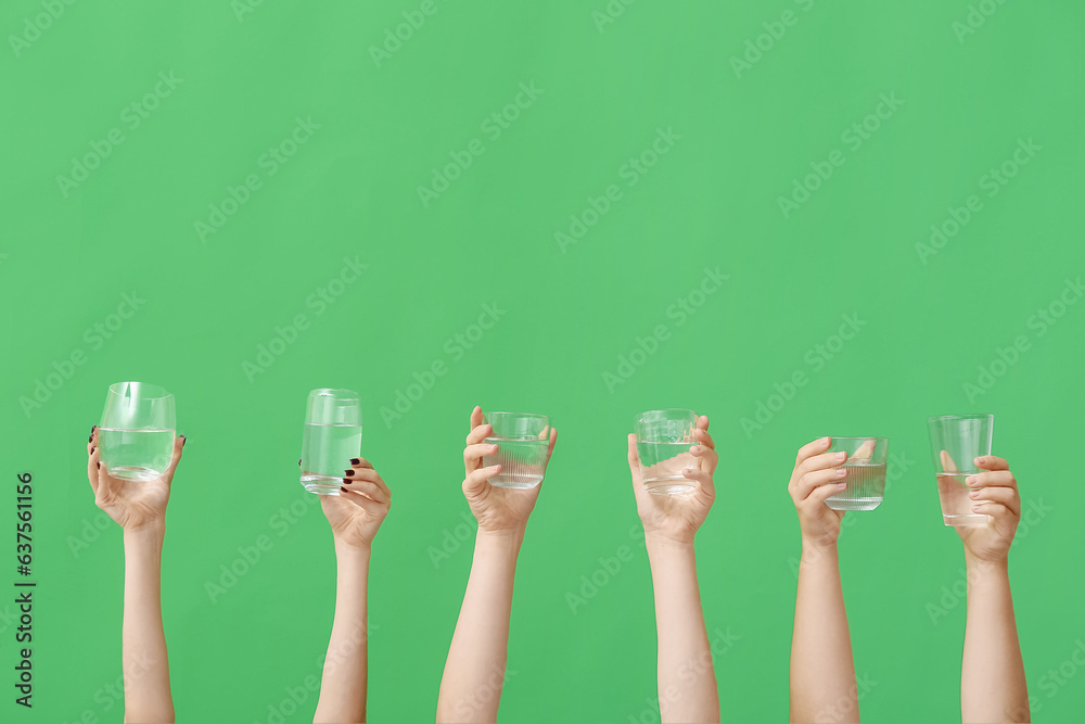 Female hands holding glasses of water on green background