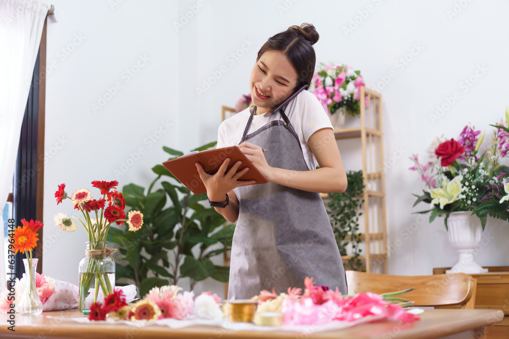 Flower shop concept, Female florist holds phone between face and shoulder to talking with customer