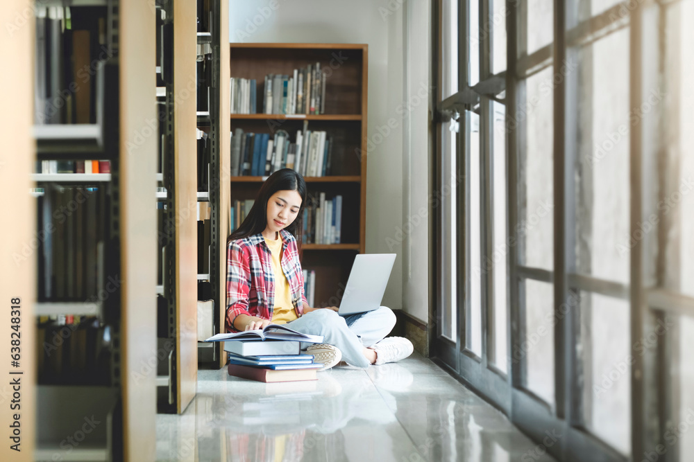 Young university student using laptop for online learning, searching and learning at library.