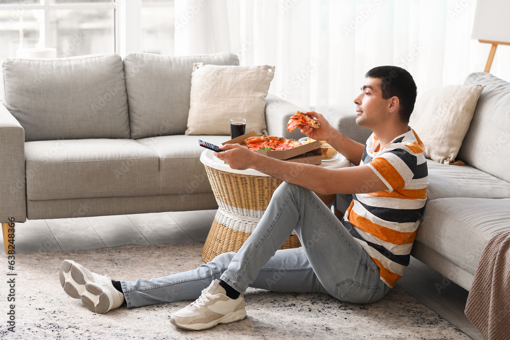 Young man with tasty pizza watching TV at home