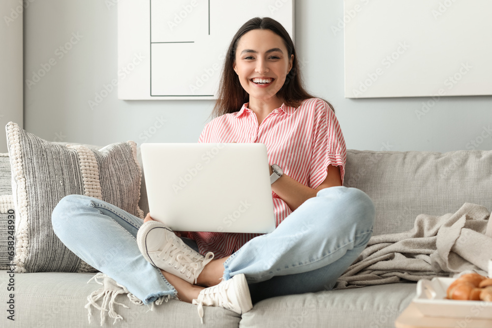 Young woman with wristwatch using laptop on sofa at home