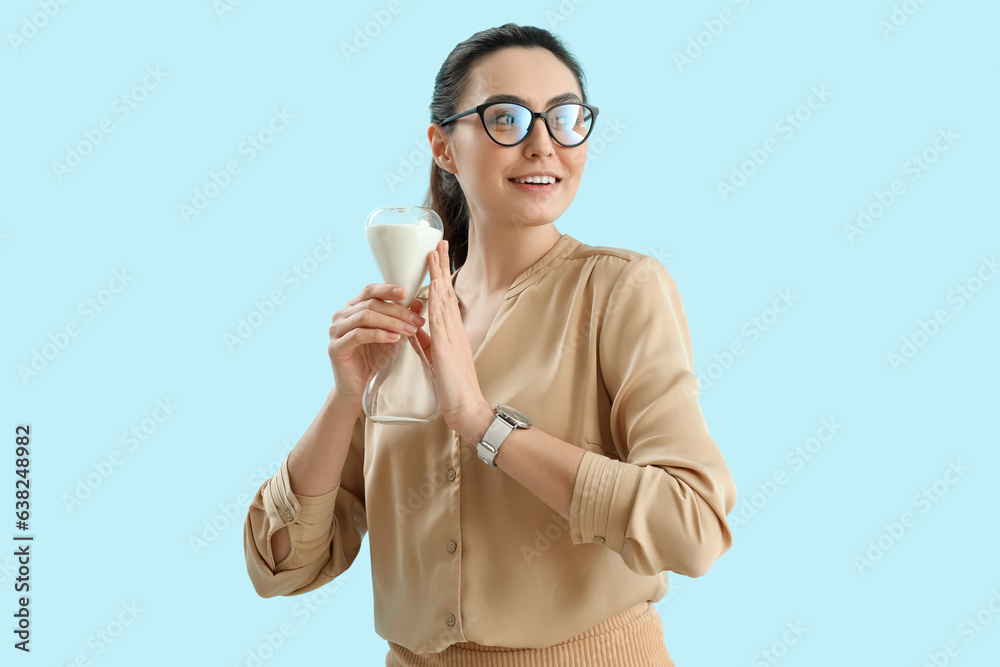 Young woman with wristwatch and hourglass on blue background