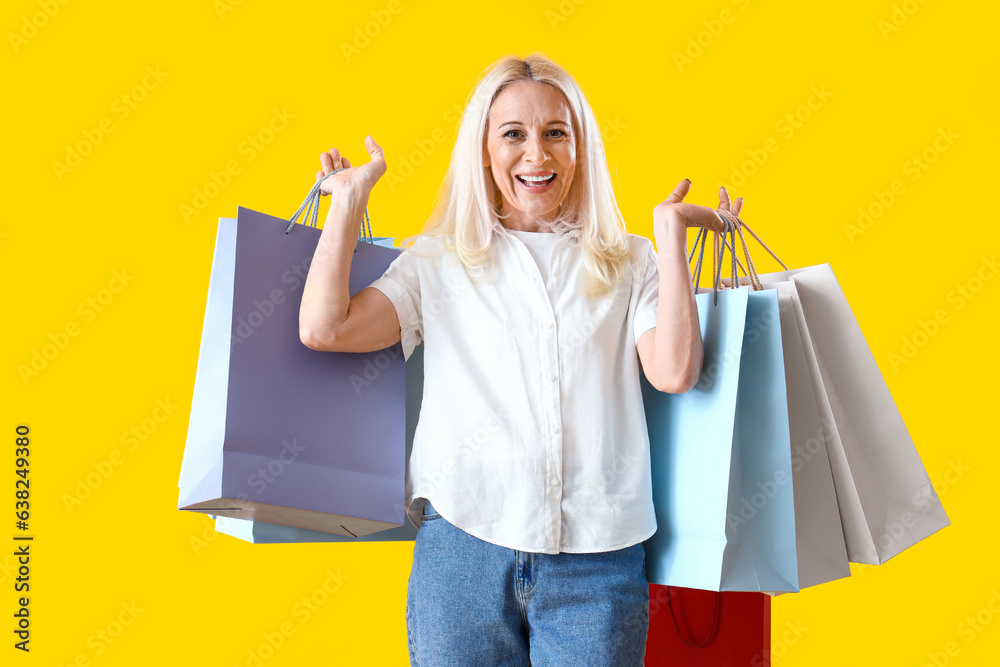 Mature woman with shopping bags on yellow background