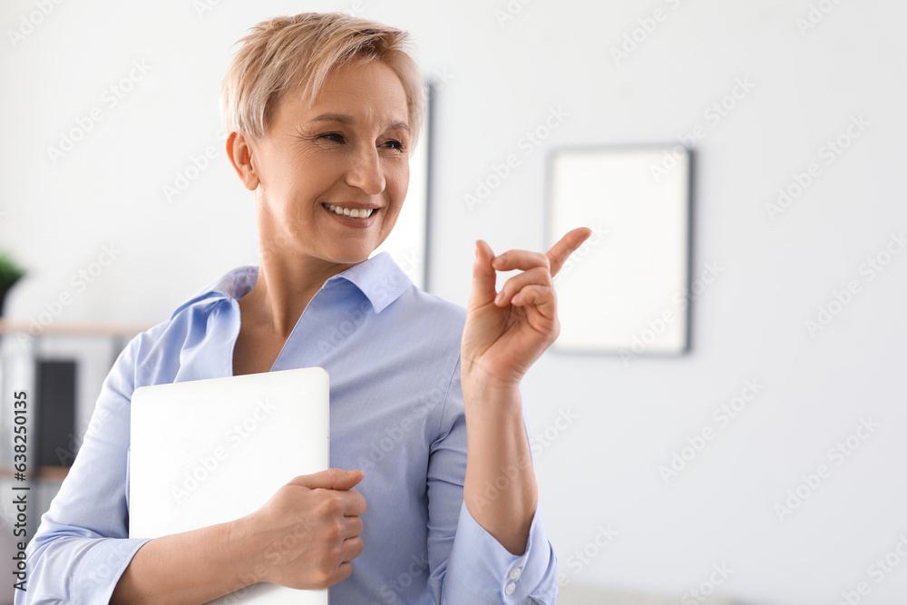 Mature businesswoman with laptop pointing at something in office