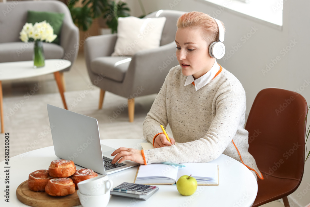 Female student in headphones studying with laptop at home