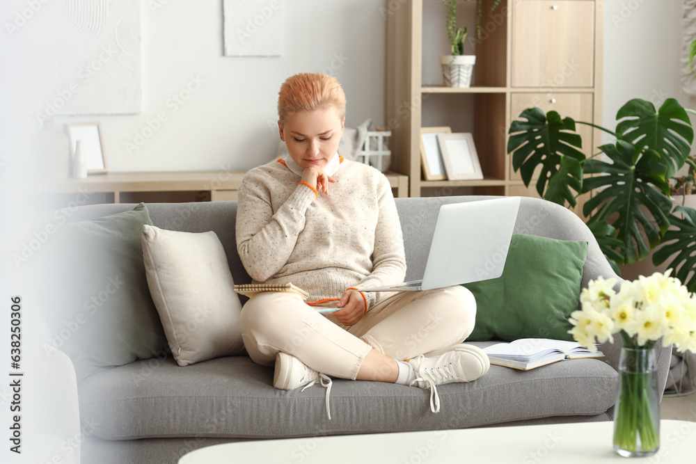 Female student studying with laptop on sofa at home