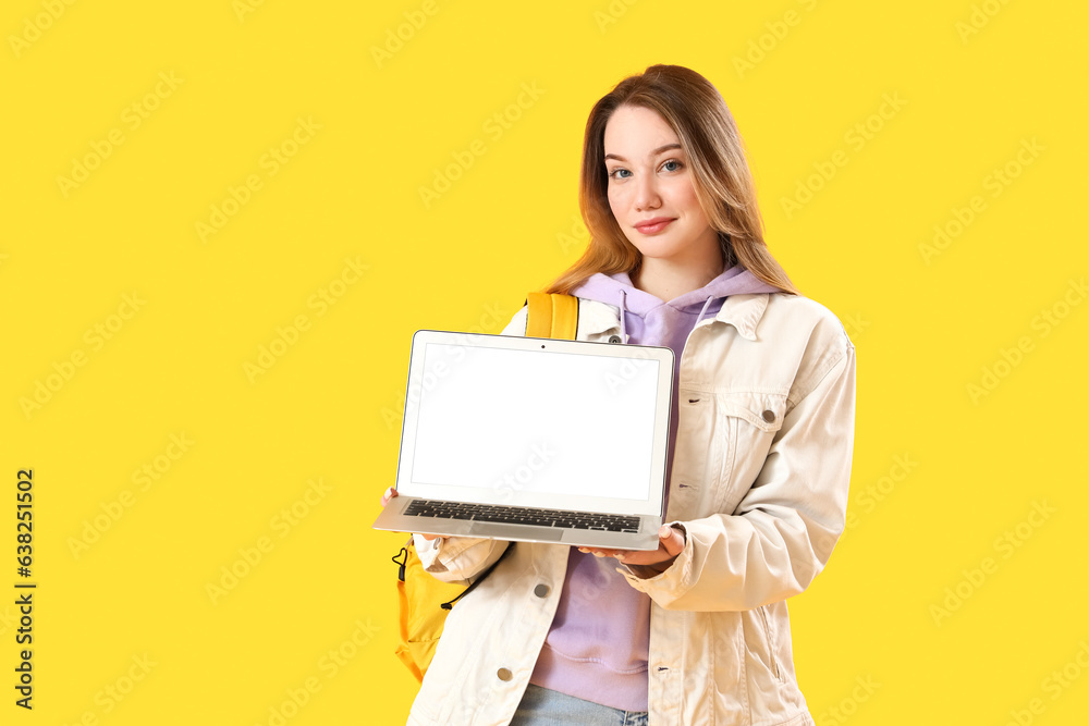 Female student with laptop on yellow background