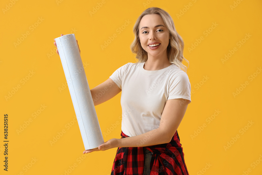 Young woman with wallpaper roll on yellow background