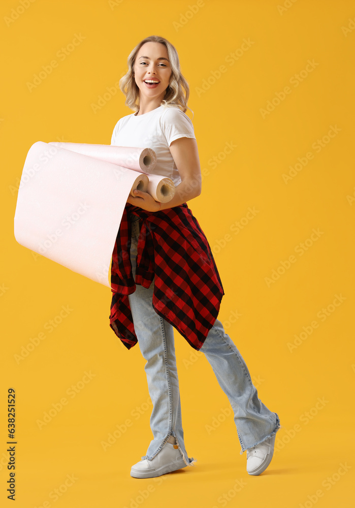 Young woman with wallpaper rolls on yellow background