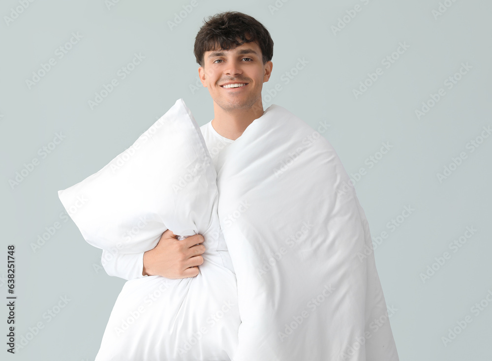 Handsome happy man with soft blanket and pillow on grey background