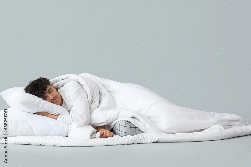 Handsome man with soft blanket and pillow sleeping on grey background