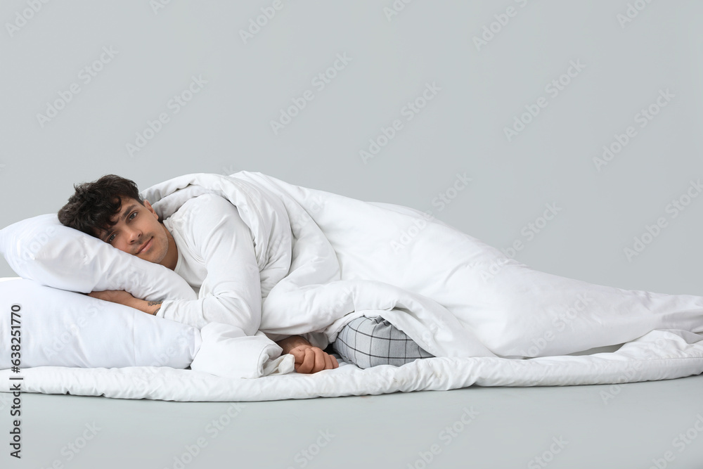 Handsome happy man with soft blanket and pillow lying on grey background