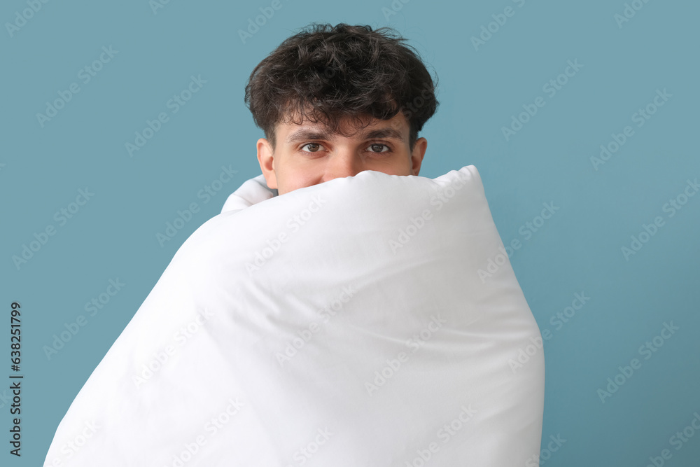 Handsome young man wrapped in soft blanket on blue background