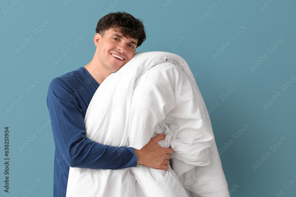 Handsome happy young man with soft blanket on blue background