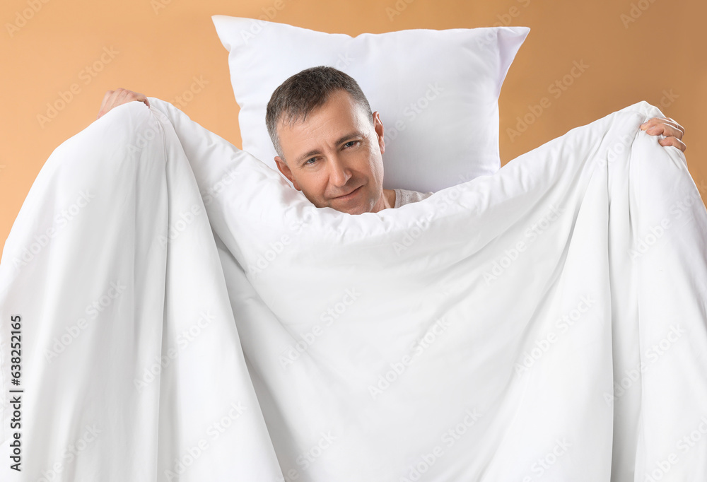 Mature man with soft pillow and blanket on beige background