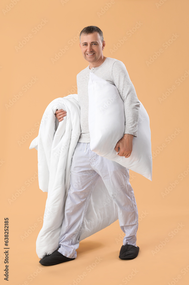 Mature man with soft pillow and blanket on beige background