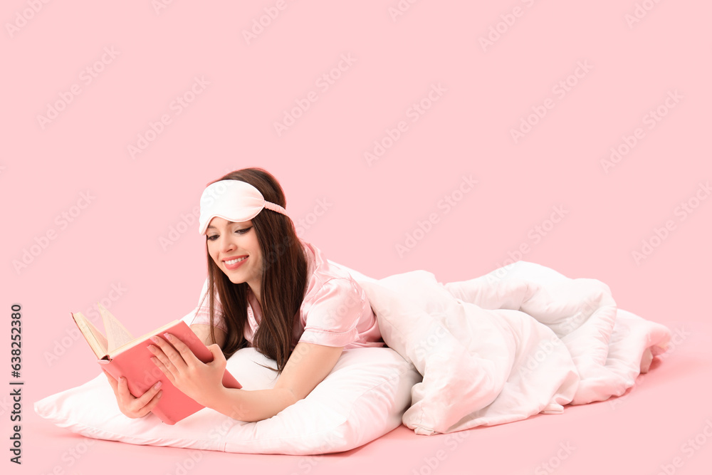 Young woman with soft blanket reading book on pink background