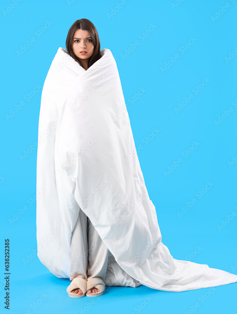 Sleepy young woman with soft blanket on blue background