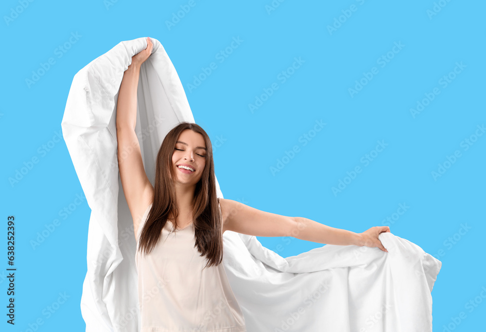 Young woman in pajamas with soft blanket on blue background