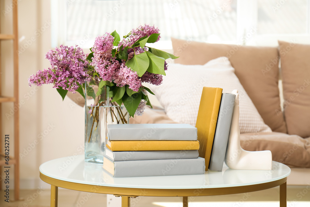 Stylish holder for books with vase of beautiful lilac flowers on coffee table in living room