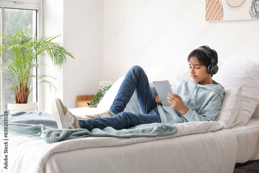 Little boy with headphones using tablet computer in bedroom