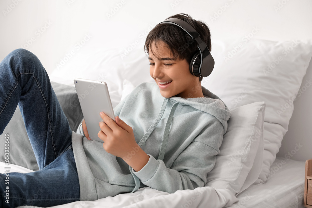 Little boy with headphones using tablet computer in bedroom