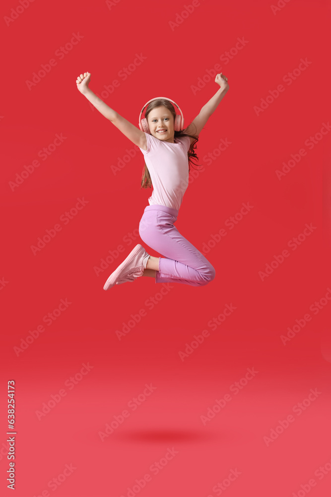 Little girl in headphones jumping on red background