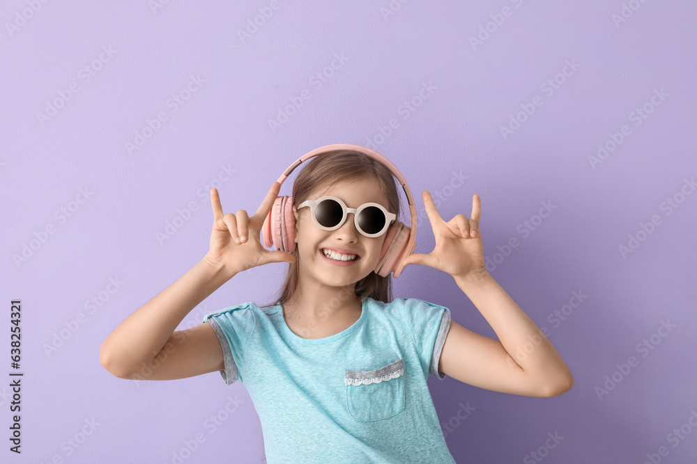 Little girl in headphones showing  devil horns  on lilac background