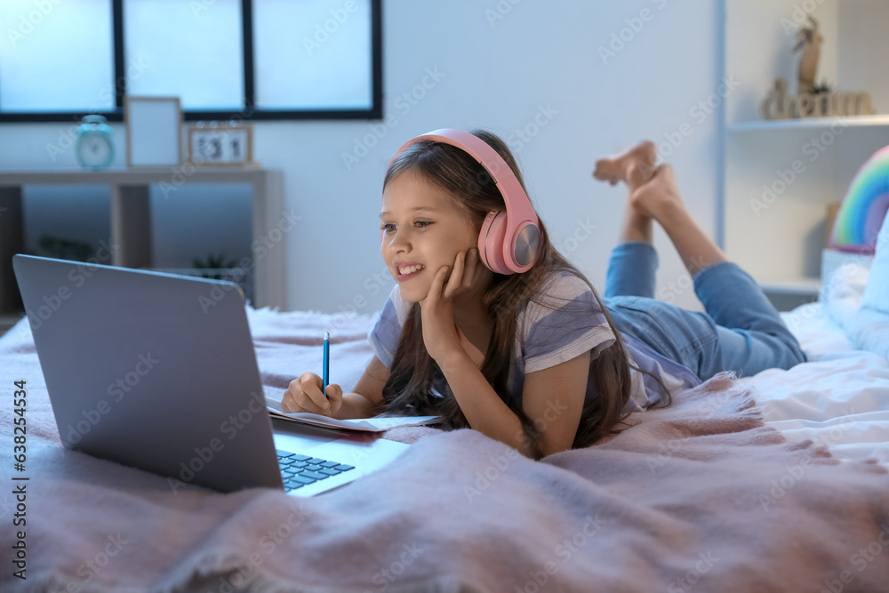 Little girl with headphones studying online in bedroom at night