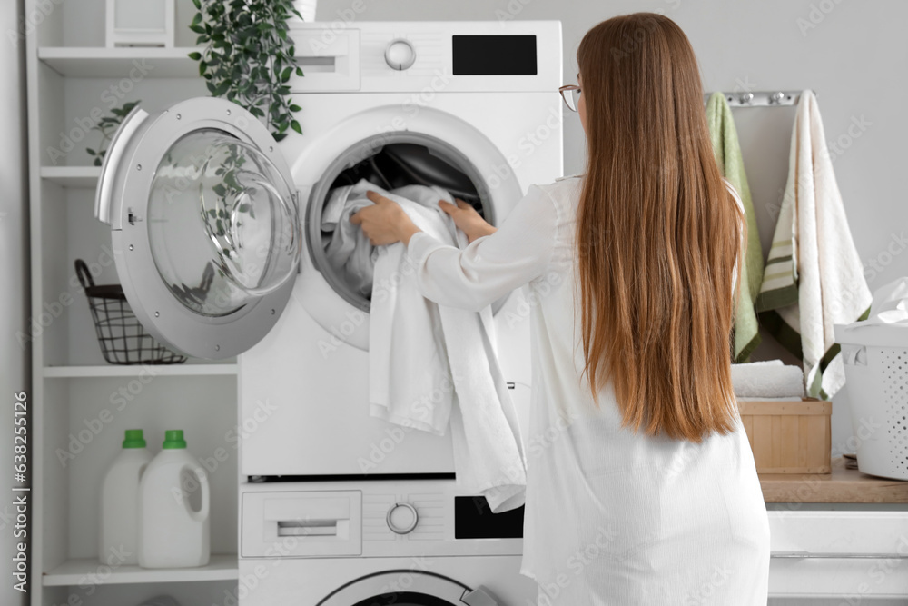 Woman putting dirty clothes into washing machine in laundry room