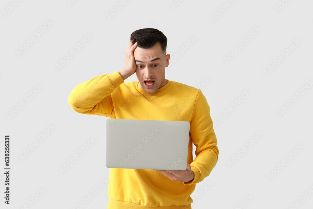 Stressed young man with laptop on light background. Deadline concept