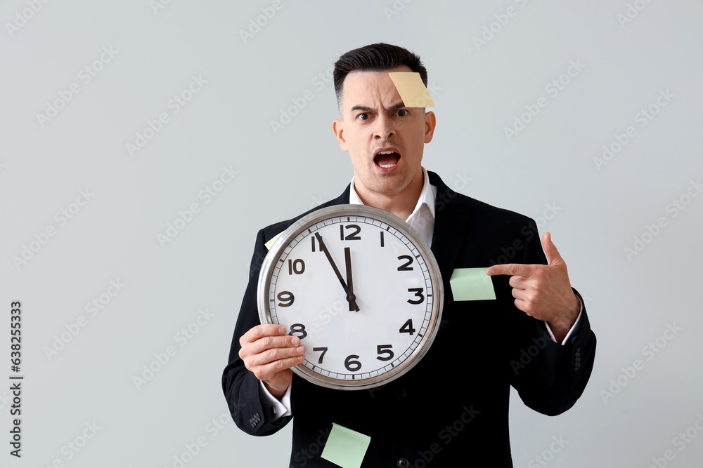 Stressed businessman with sticky notes and clock on light background. Deadline concept