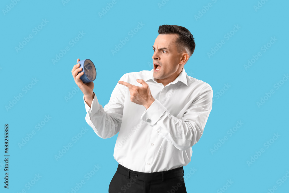 Stressed businessman pointing at clock on blue background. Deadline concept